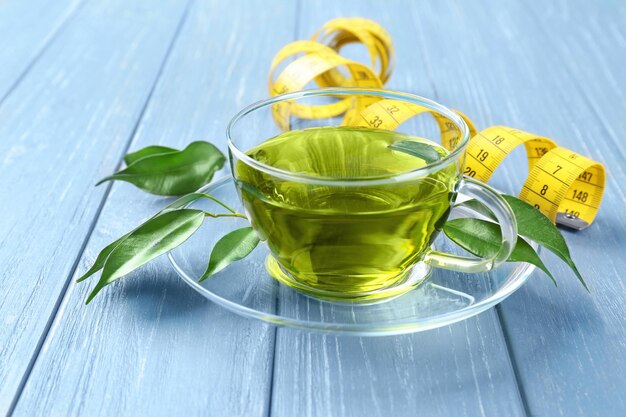 a cup of green tea with measuring tape and leaves at its one side.