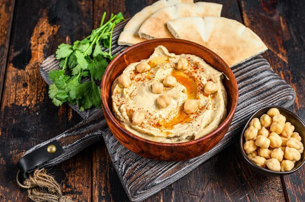 hummus in a brown bowl is placed with coriander and bread.