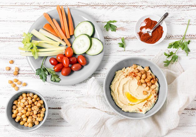 Hummus in a bowl is placed with veggies and legumes.