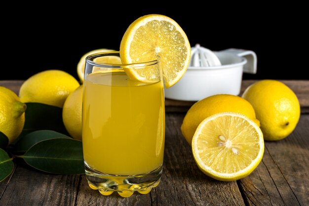 lemon juice glass wit lemon scattered around it on a wooden table.
