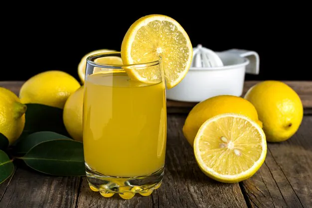 a glass of lemon juice with lemon slices placed aside on the wooden table.