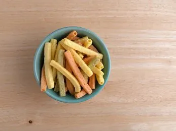 veggie straws in a blue bowl on wooden surface